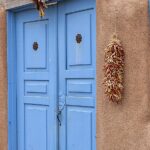 Blue doors of an old adobe house in Taos, New Mexico. Hanging peppers and indian corn.