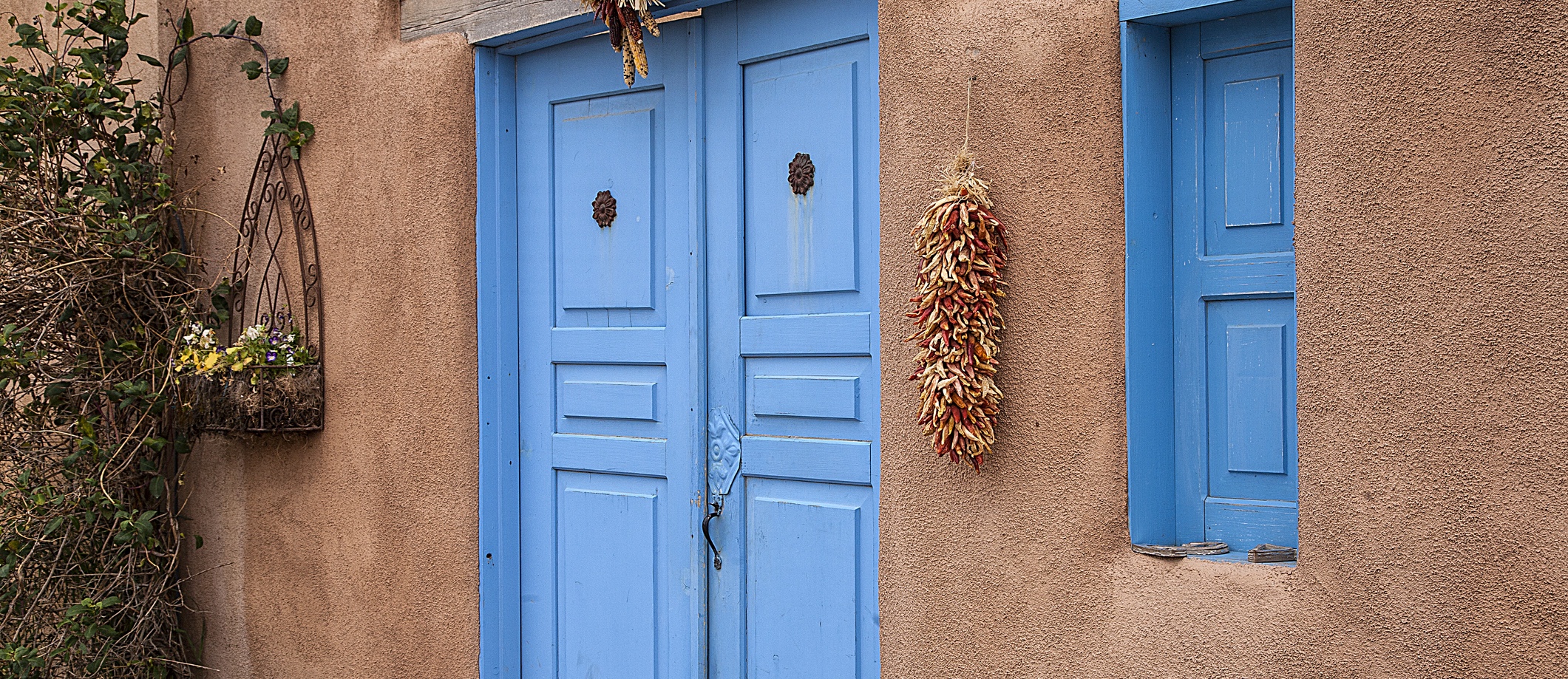Blue doors of an old adobe house in Taos, New Mexico. Hanging peppers and indian corn.